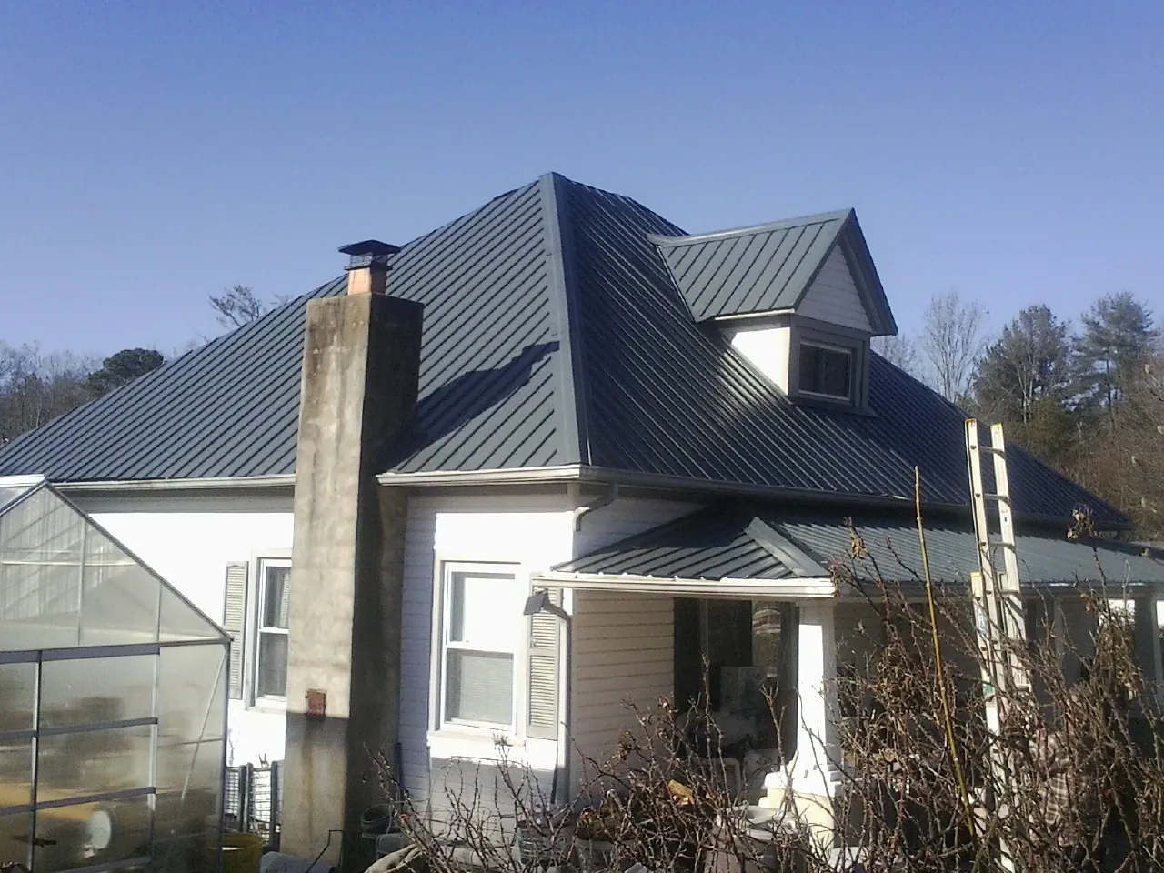 Dark blue standing seam metal roof on a white farmhouse with dormer — Slate & Tile Roof Repair by Roofing Brothers in Denison