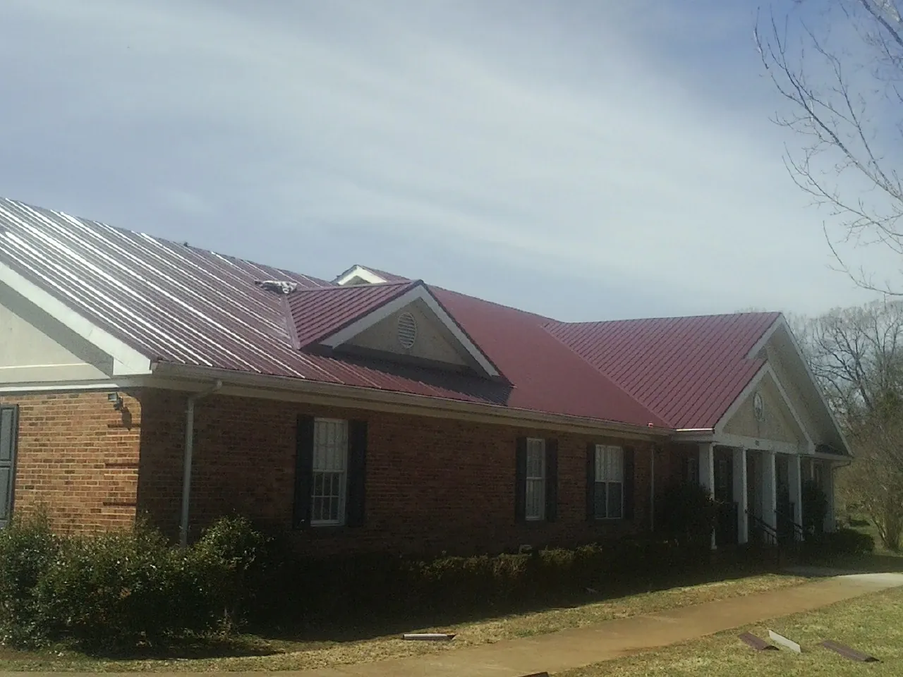 Red metal roof with gabled entries on a long brick building, from a Hail Damage Roof Repair job in Denison