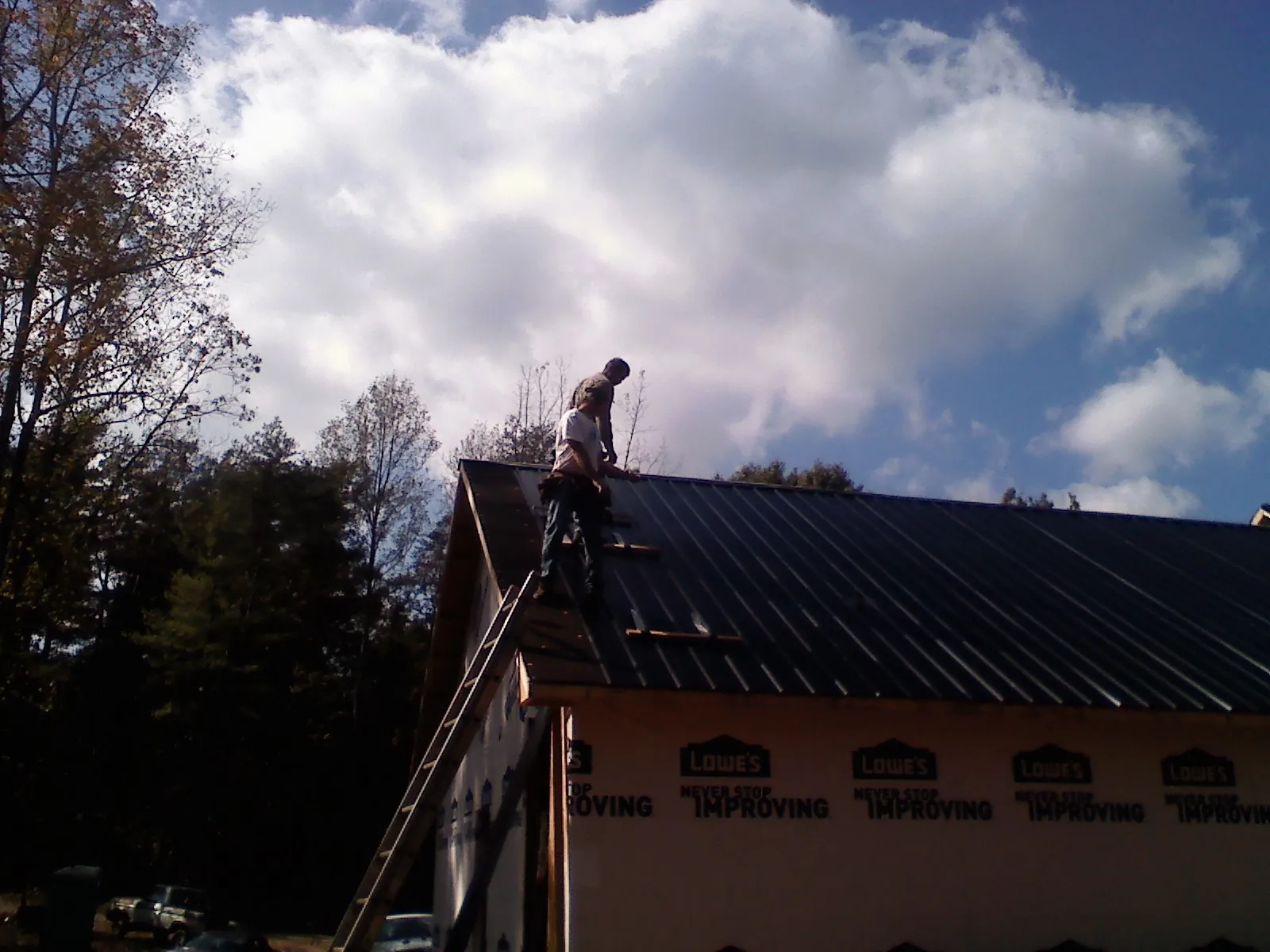 Roofer fastening dark metal panels high against a cloudy sky, from a Roof Inspection job in Denison