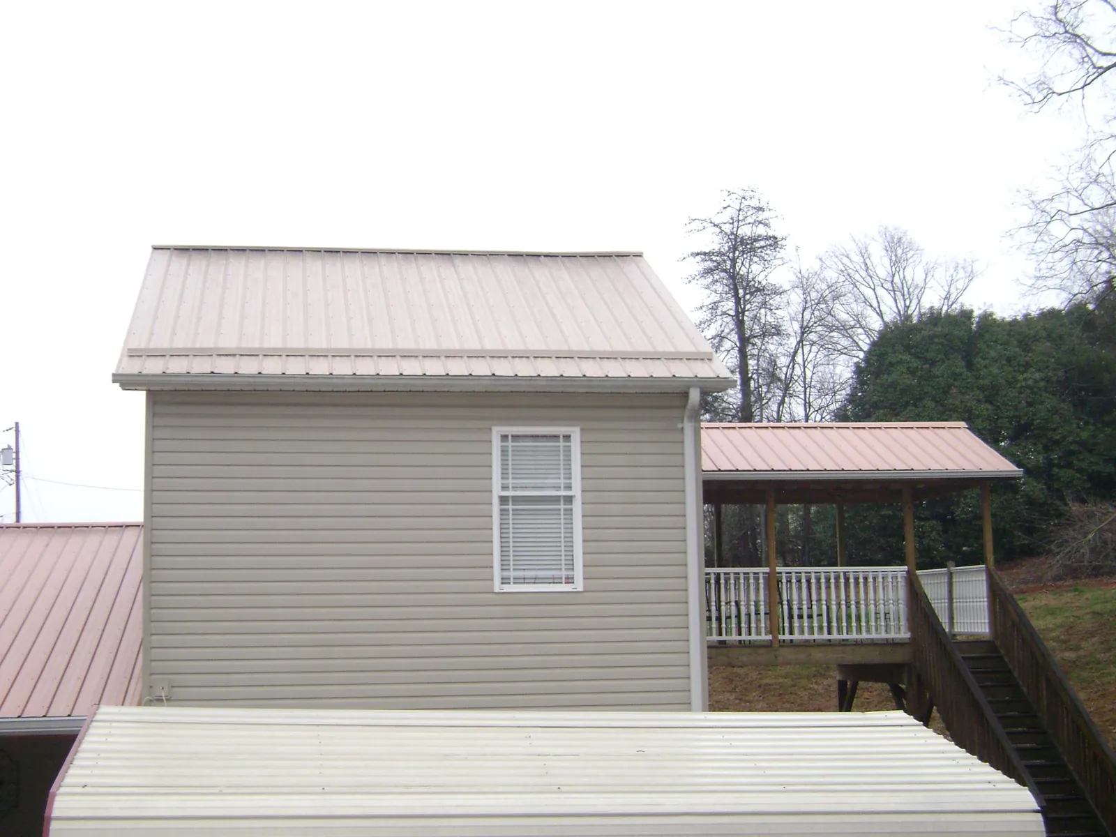 Tan metal roofs on a two story addition and attached porch, from a Roof Replacement job in Denison